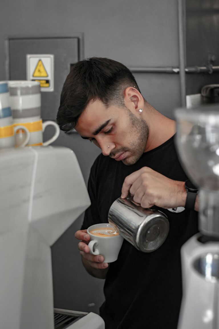 Focused barista makes latte art in a stylish café setting, pouring milk into espresso.